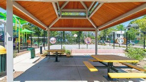 Ein überdachter Picknickbereich mit Bänken und einem Spielplatz im Hintergrund.