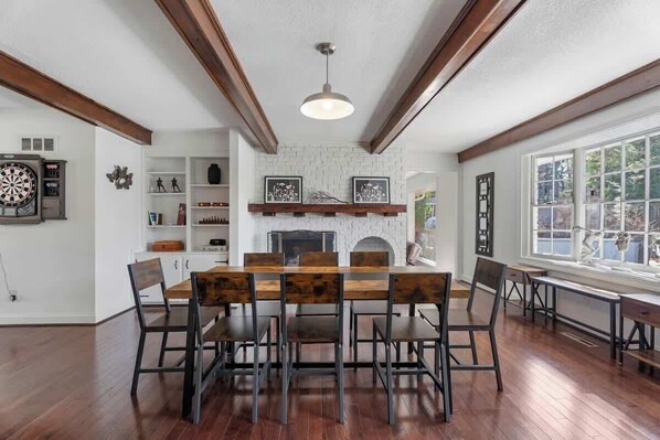 Un coin repas avec une table et des chaises en bois, une cheminée et un jeu de fléchettes accroché au mur.