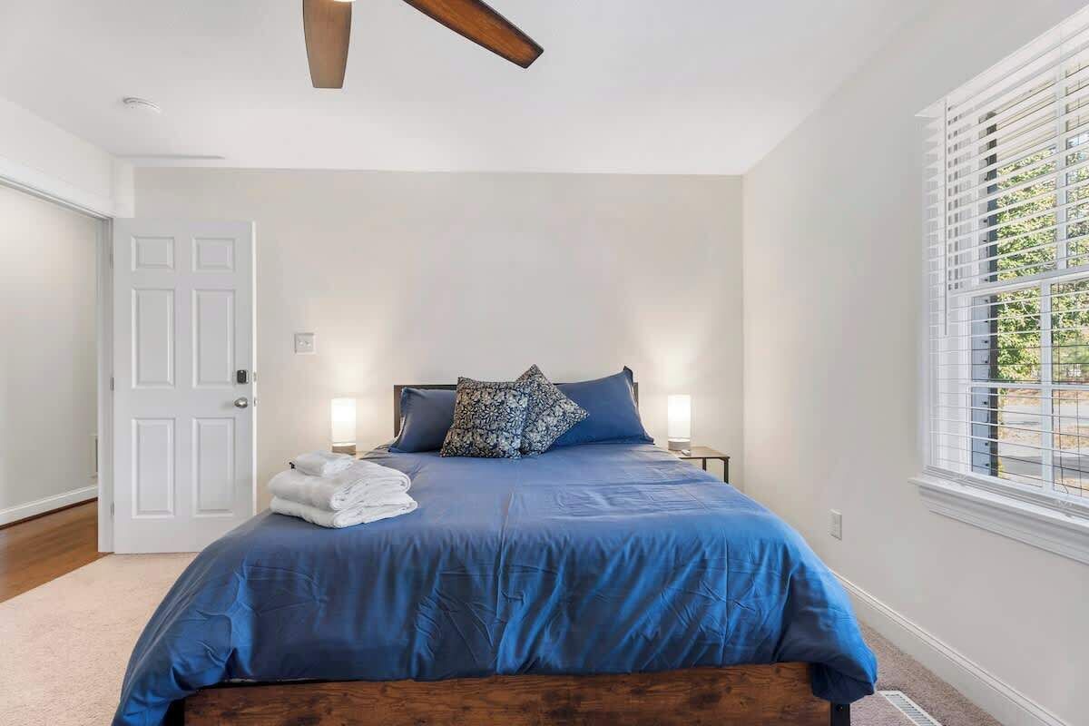 Een slaapkamer met een bed, nachtlampjes, een deur en een raam met jaloezieën.