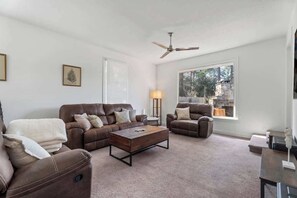 Un salon avec un canapé en cuir marron, un fauteuil assorti, une table basse en bois et un ventilateur de plafond.