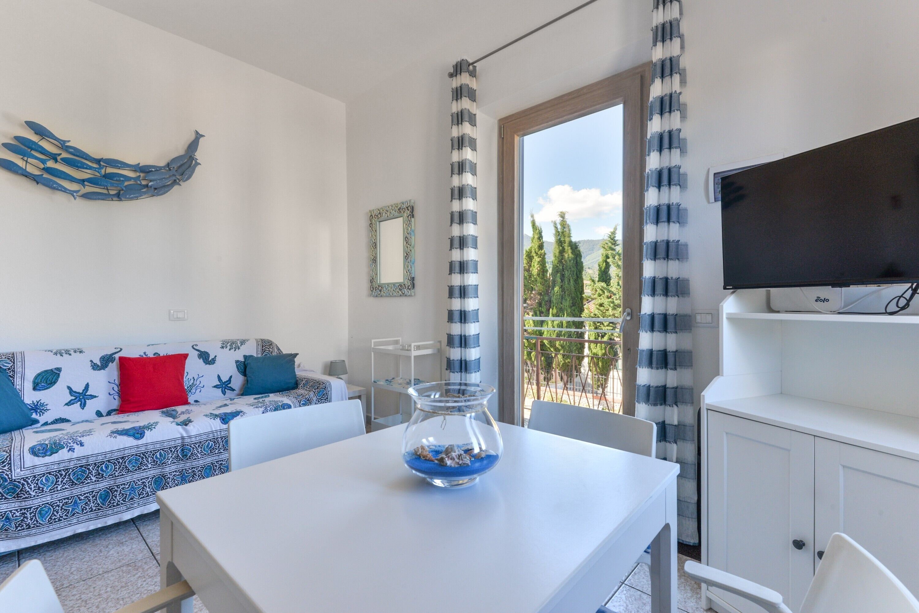 Un salon moderne avec un canapé, une table basse en verre, un téléviseur et un balcon agrémenté de rideaux.