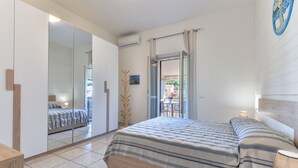 Una camera da letto con un letto, un armadio, uno specchio e vista attraverso una porta aperta.