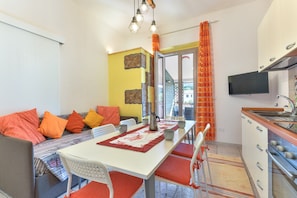 Un espacio habitable compacto con comedor, kitchenette y sofá con cojines naranja.