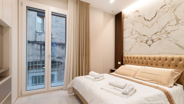Ein Hotelzimmer mit Bett, einem fenster mit Vorhängen, einer Marmorwand und Blick ins Freie.