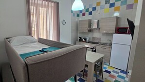 Een compacte kamer met een bed, een klein tafeltje, een kitchenette en een raam met gordijnen.