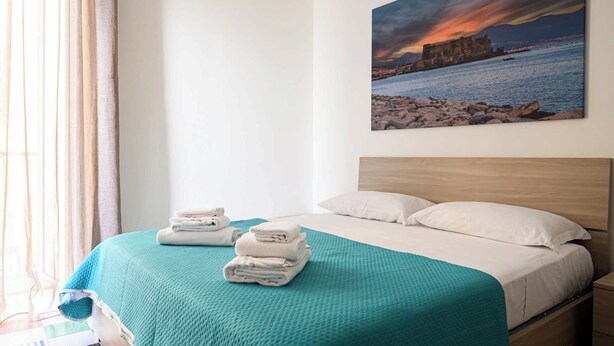Een hotelkamer met een bed, een schilderij van een zonsondergang boven een rotsachtige kustlijn en een raam met gordijnen.