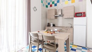 Een moderne keuken met een eettafel, stoelen, een magnetron, een koelkast en een kleurrijke tegelachterwand.