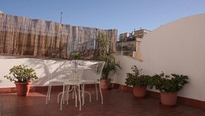 Um pátio com uma mesa e cadeiras, rodeado por vasos de plantas.