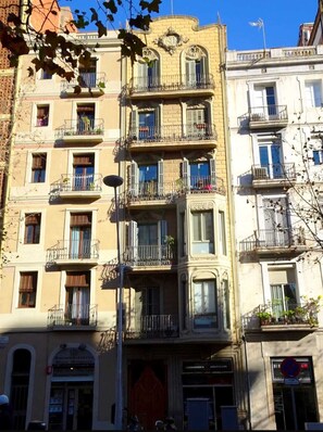A multi-story building with balconies, a shop at the ground level, and a sign indicating a 4-hour parking limit. - Urgell - Lovely apartment with a terrace (Barcelona)