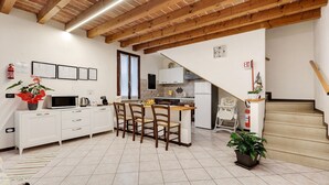 A kitchen with a dining area, wooden ceiling beams, white cabinetry, and a potted plant. - Apartment 'Il Vagabondo' with Wi-Fi and Air Conditioning (Volta Mantovana)