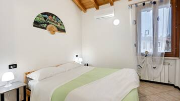 A bedroom with a bed, bedside tables, a wall-mounted fan, an air conditioning unit, and a window with curtains.