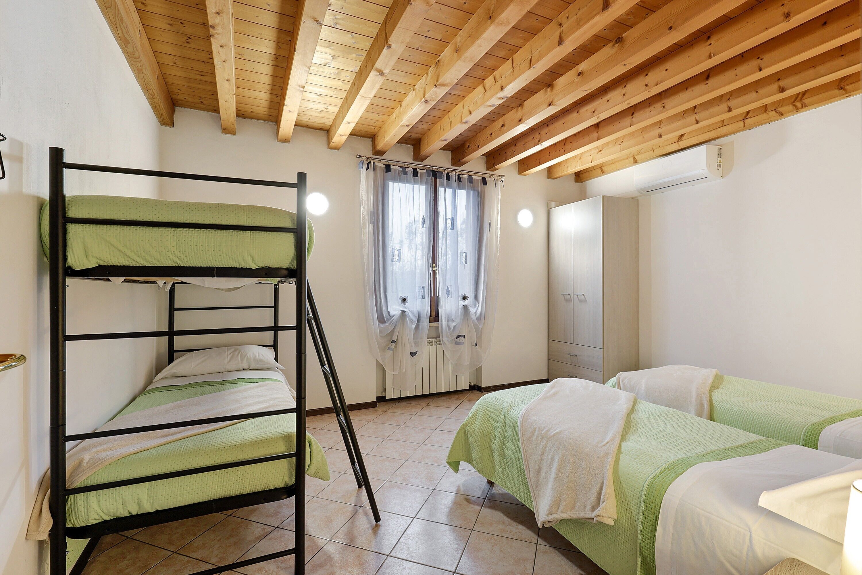 Una camera del dormitorio con letti a castello, soffitto in legno, una finestra con tende e un armadio bianco.