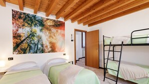 A room with two beds, a bunk bed, wooden ceiling beams, a large painting, and a door leading to another room. - Apartment 'Il Vagabondo' with Wi-Fi and Air Conditioning (Volta Mantovana)