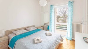 Une chambre à coucher comprenant un lit, une table de chevet, une commode, une fenêtre avec des rideaux et un radiateur.