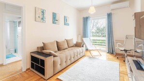 Un salon moderne avec un canapé, une petite table, un fauteuil et une vue sur l’extérieur.