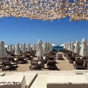 A beach with rows of sun loungers and umbrellas, a clear sky, and the ocean in the background. - Beachside Apartment - Available per month (Voula)