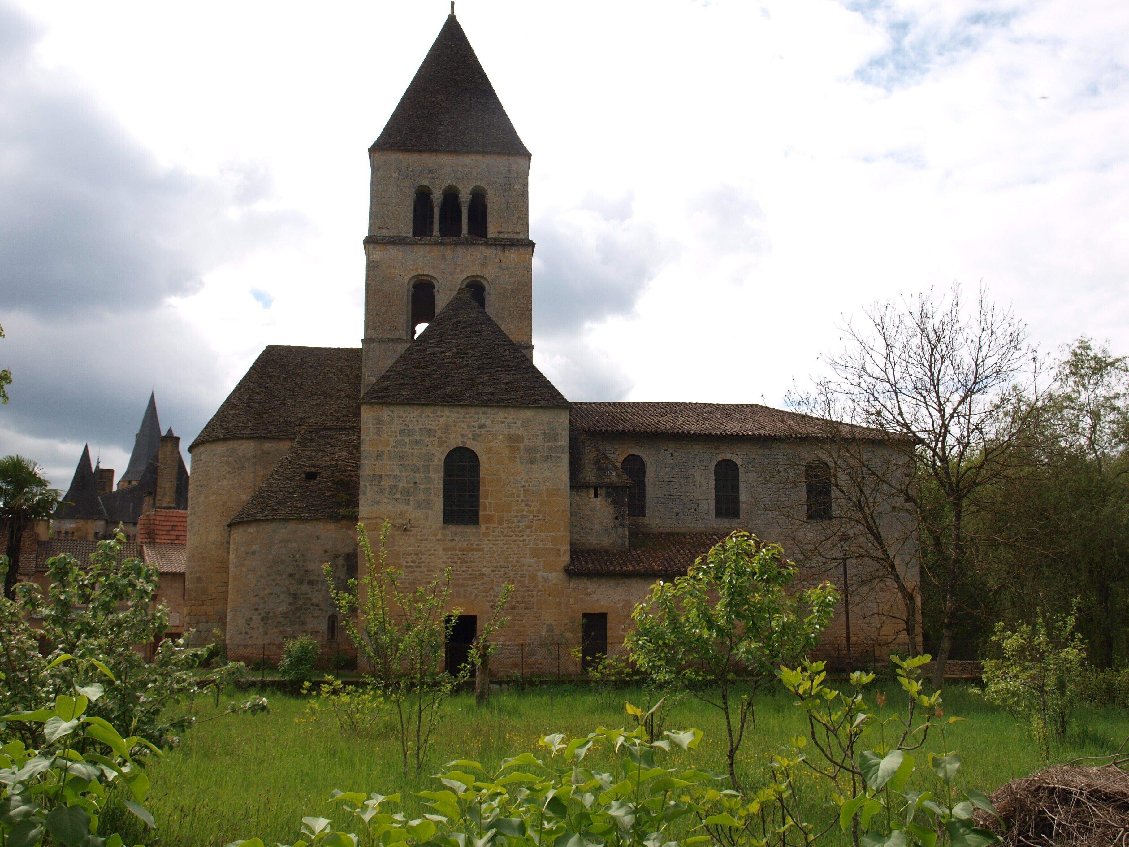 Eine historische Steinkirche mit einem Glockenturm, umgeben von Grünflächen und anderen Gebäuden.