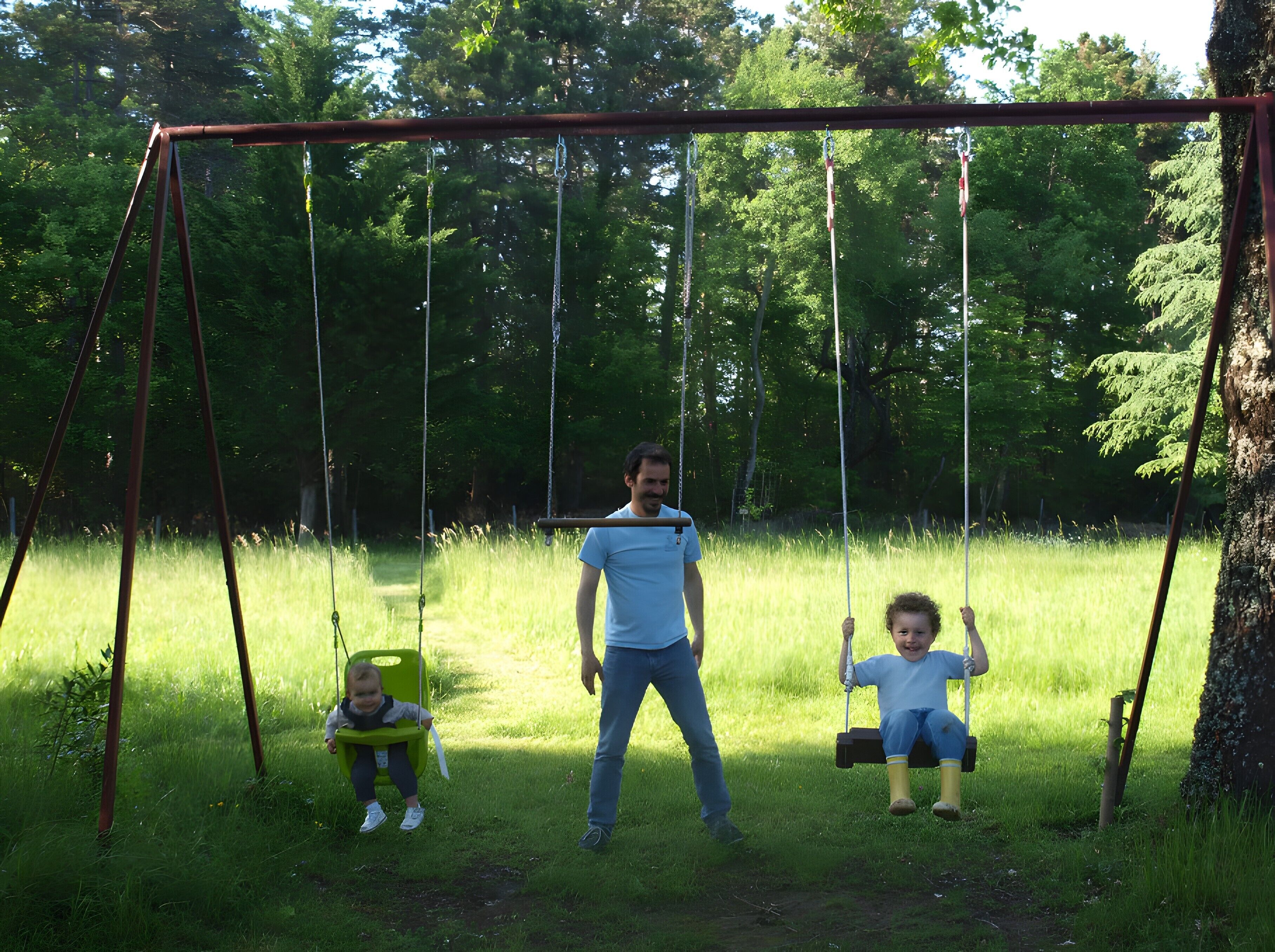 A swing set in a grassy area with trees in the background.