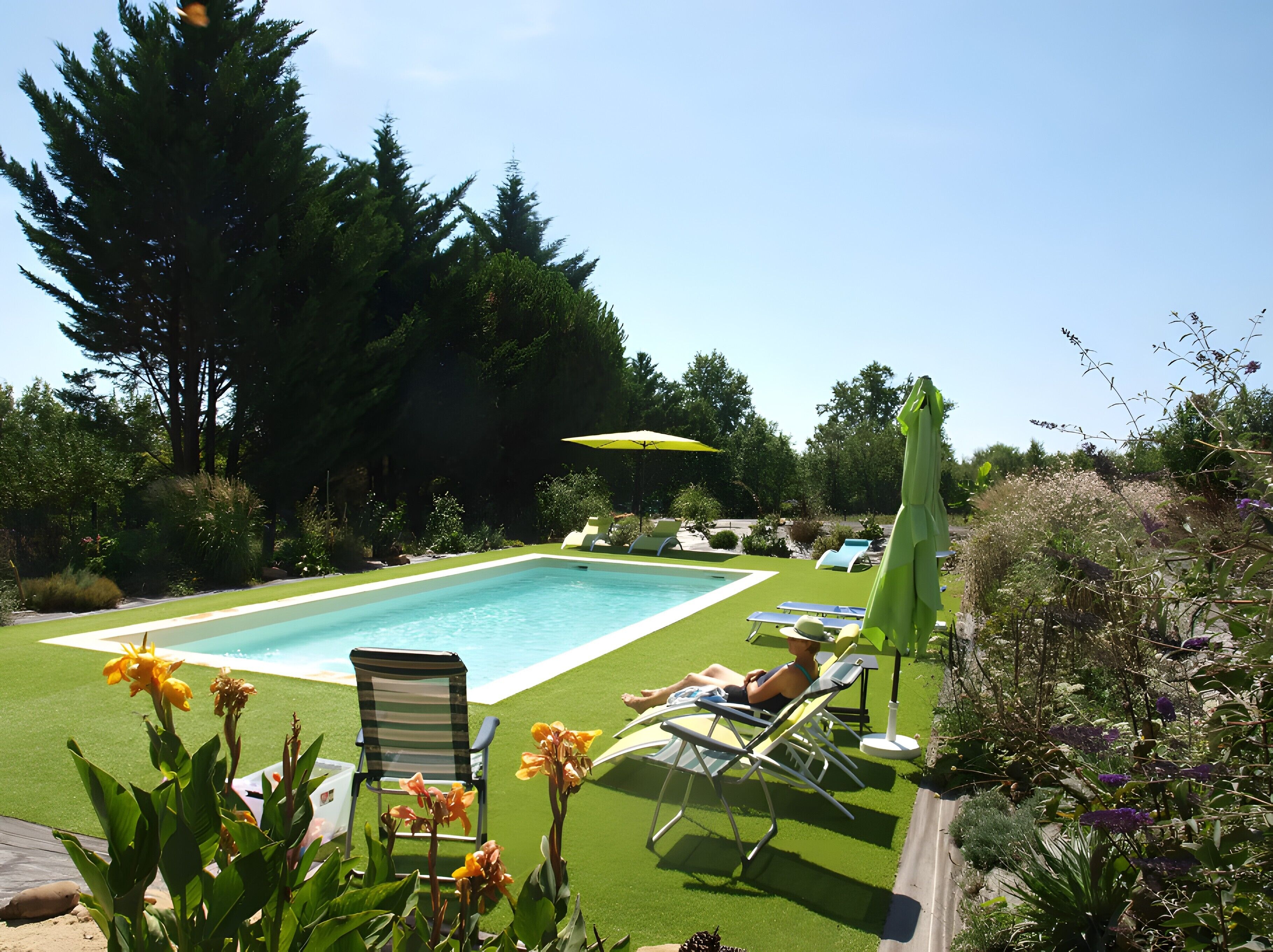 A rectangular pool with surrounding lounge chairs and a green umbrella.