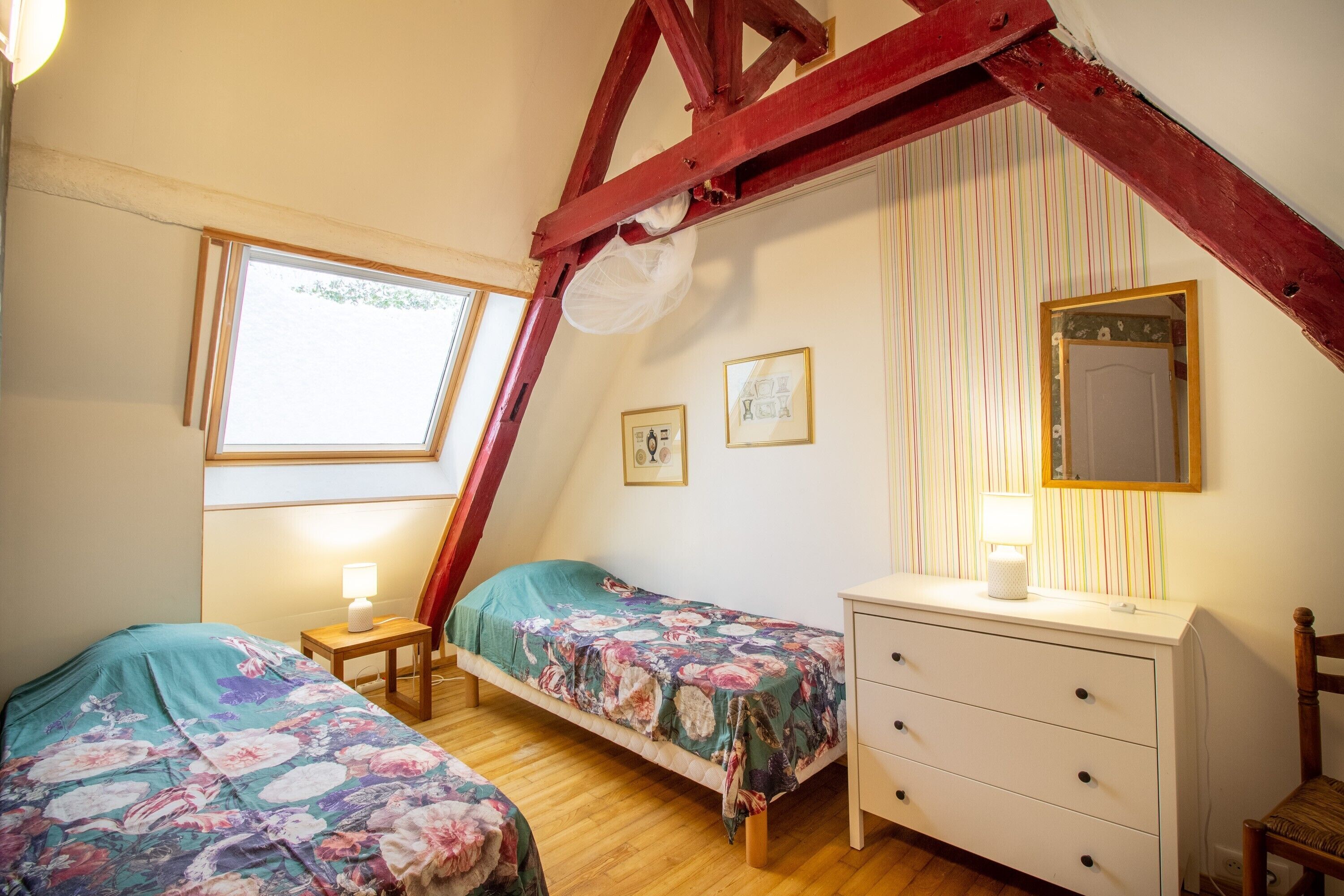 A bedroom with two single beds, a dresser, a mirror, and a window.