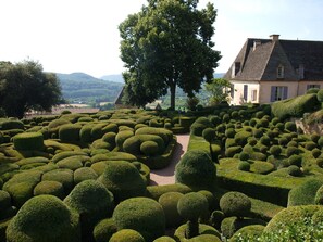 Un jardin aménagé avec le plus grand soin, doté de haies taillées de manière géométrique, d’un arbre remarquable et d’un bâtiment dont le toit est en pente.