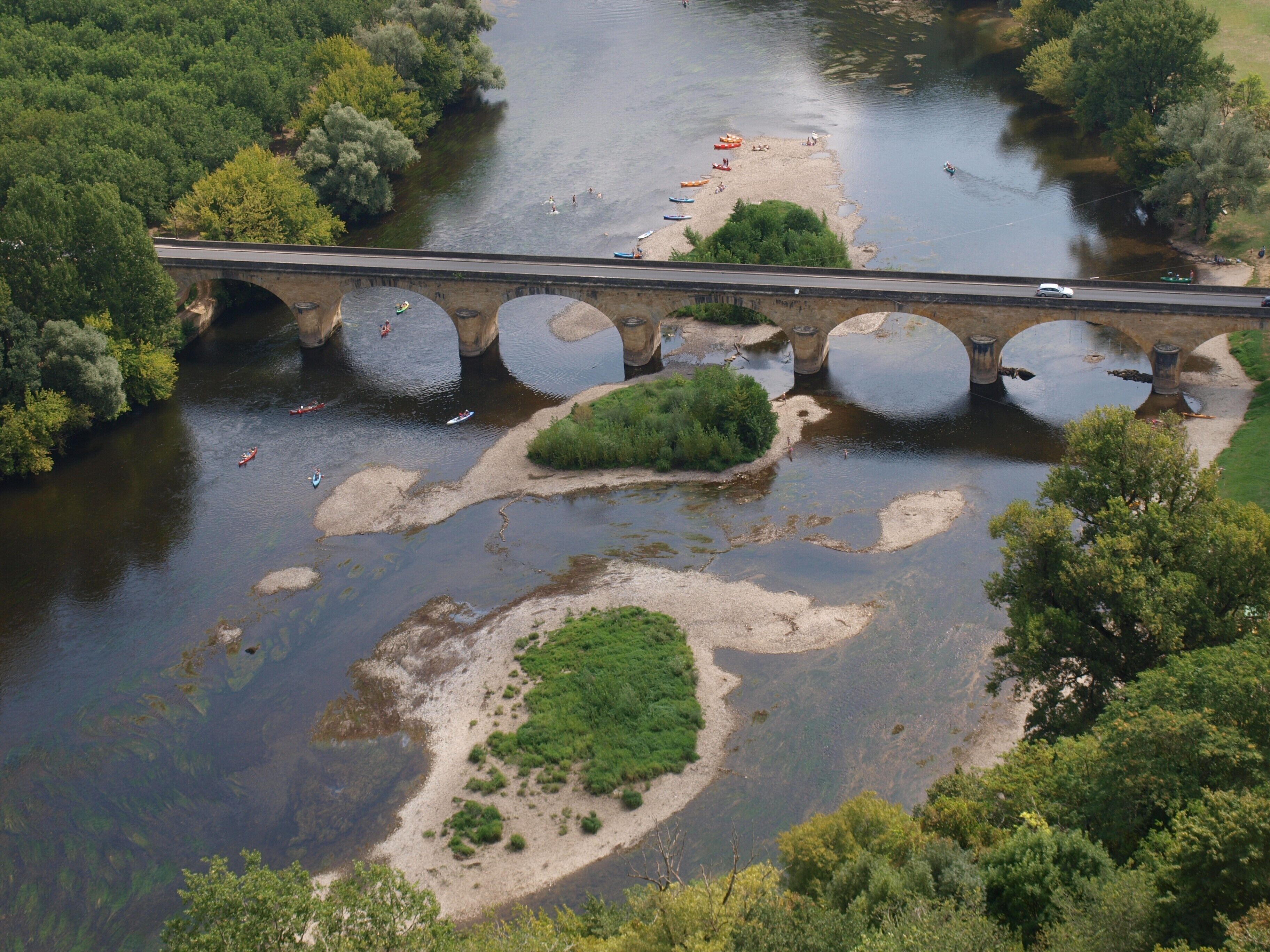 Une rivière avec des bateaux, un pont et de la verdure.