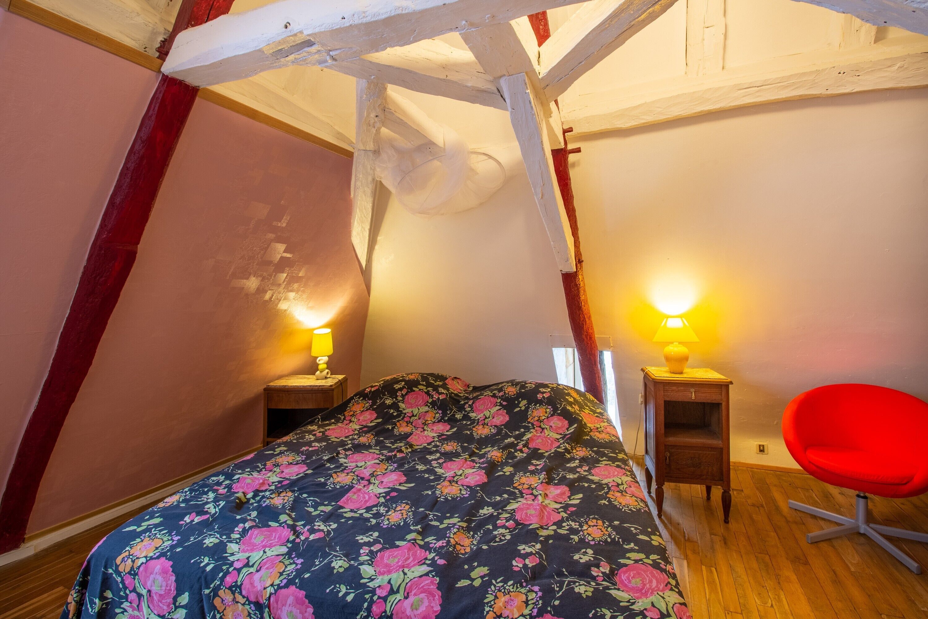 Une chambre à coucher avec un lit, deux tables de chevet, une chaise rouge et un plafond en bois.