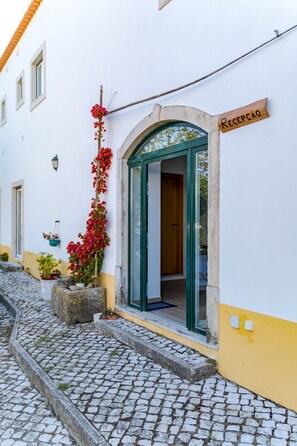 A building with a reception area, cobblestone street, and potted plants. - Quinta do Oratório Agroturismo (Óbidos)