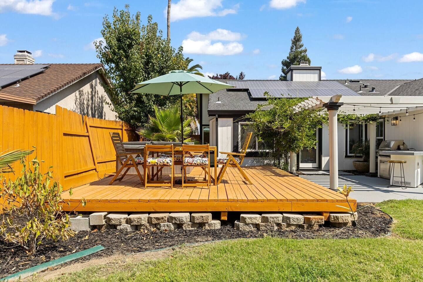 Ein Garten mit Holzterrasse, Sitzgelegenheit im Freien, Grill und einer Pergola.