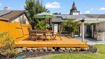 Ein Garten mit Holzterrasse, Sitzgelegenheit im Freien, Grill und einer Pergola.