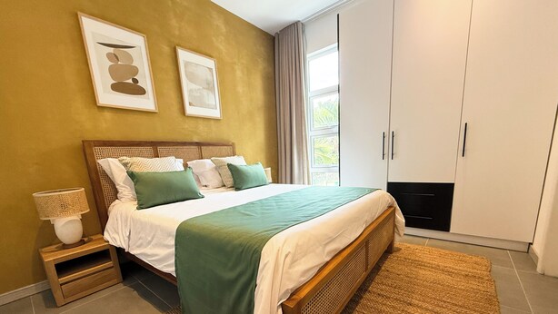 A bedroom with a bed, nightstand, lamp, artwork, wardrobe, and a view of greenery outside. - Lorlagon by LOV Mauritius  (Trou d'Eau Douce)
