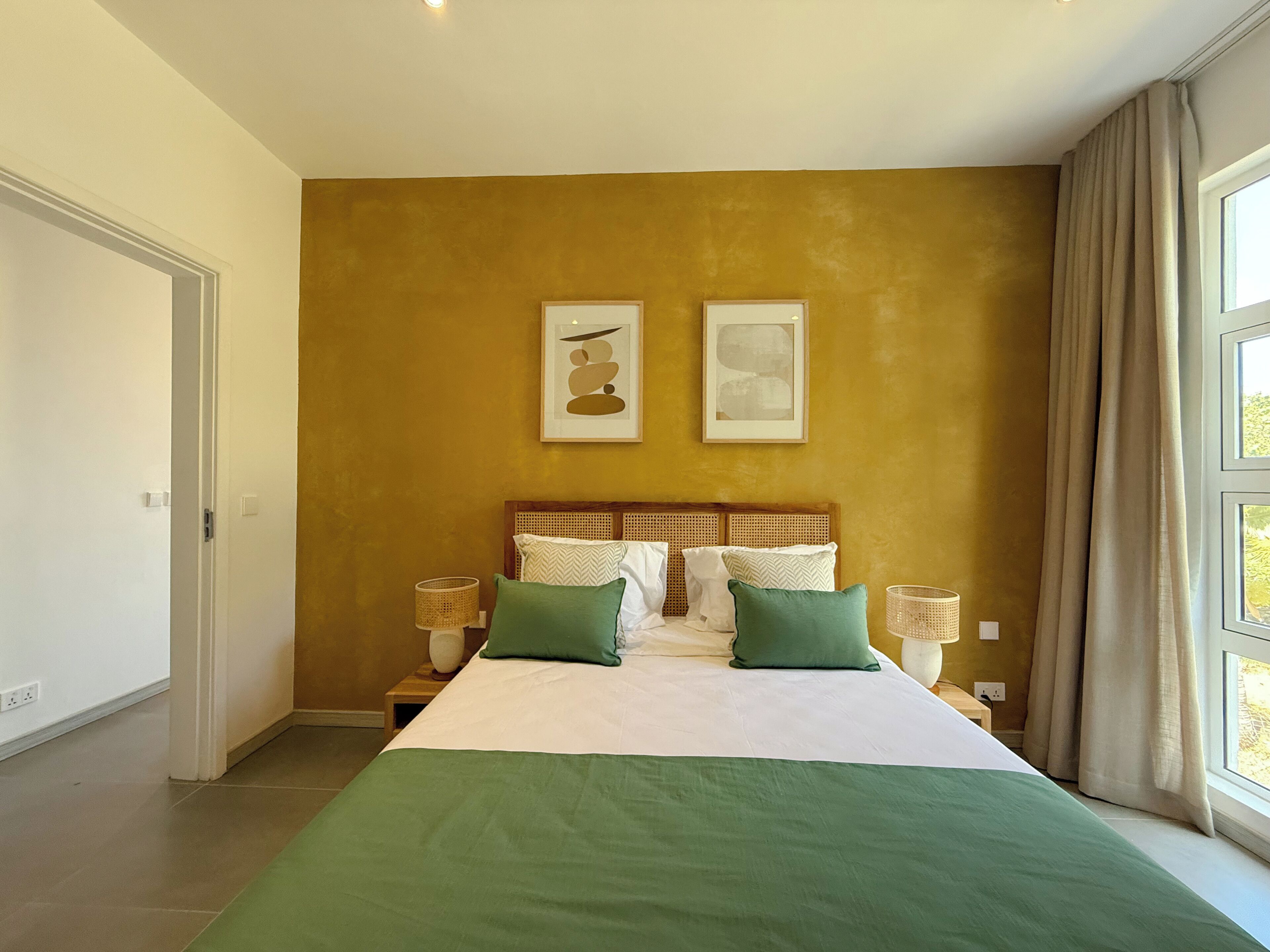 Una camera d'albergo con un letto, due comodini, una finestra con tende e un'opera d'arte appesa al muro.