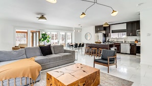 A modern living room with a grey sofa, a wooden coffee table, and a dining area with chairs.