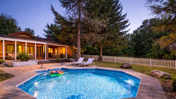 A rectangular swimming pool with a tiled edge, surrounded by a concrete deck. There are lounge chairs and a small inflatable pool float.