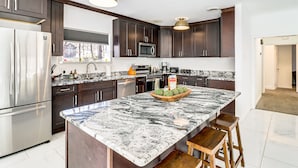 A modern kitchen with dark wood cabinets, stainless steel appliances, and a large marble island.