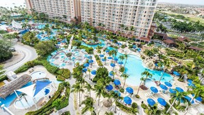 Een resort met meerdere zwembaden, palmbomen en een groot hotelgebouw.