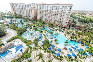 Ein Resort mit mehreren Swimmingpools, Palmen und einem großen Hotelgebäude.