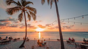 Een restaurant aan het strand met terras, palmbomen en lichtjes.