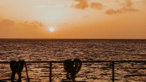 Een zonsondergang boven de oceaan, met een hekwerk op de voorgrond.
