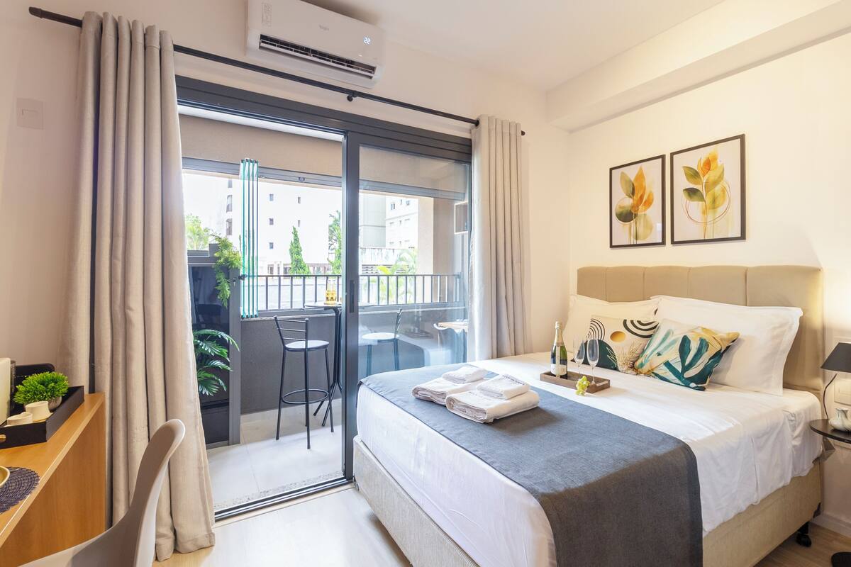 Ein Hotelzimmer mit Bett, Schreibtisch, Stuhl, einem Balkon mit Tisch und Stühlen sowie zwei gerahmten Bildern an der Wand.