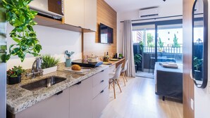 A modern kitchen with a granite countertop, stainless steel sink, and a built-in oven. There is a dining area with a table and chairs, and a sliding glass door leading to an outdoor balcony. - Vila Mariana near Ibirapuera Park (São Paulo)