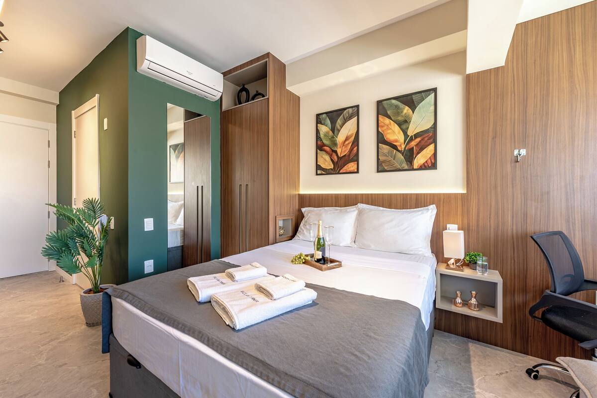 Ein modernes Hotelzimmer mit einem großen Bett, einem Nachttisch mit Lampe, einer kleinen Pflanze und einem Bild an der Wand.