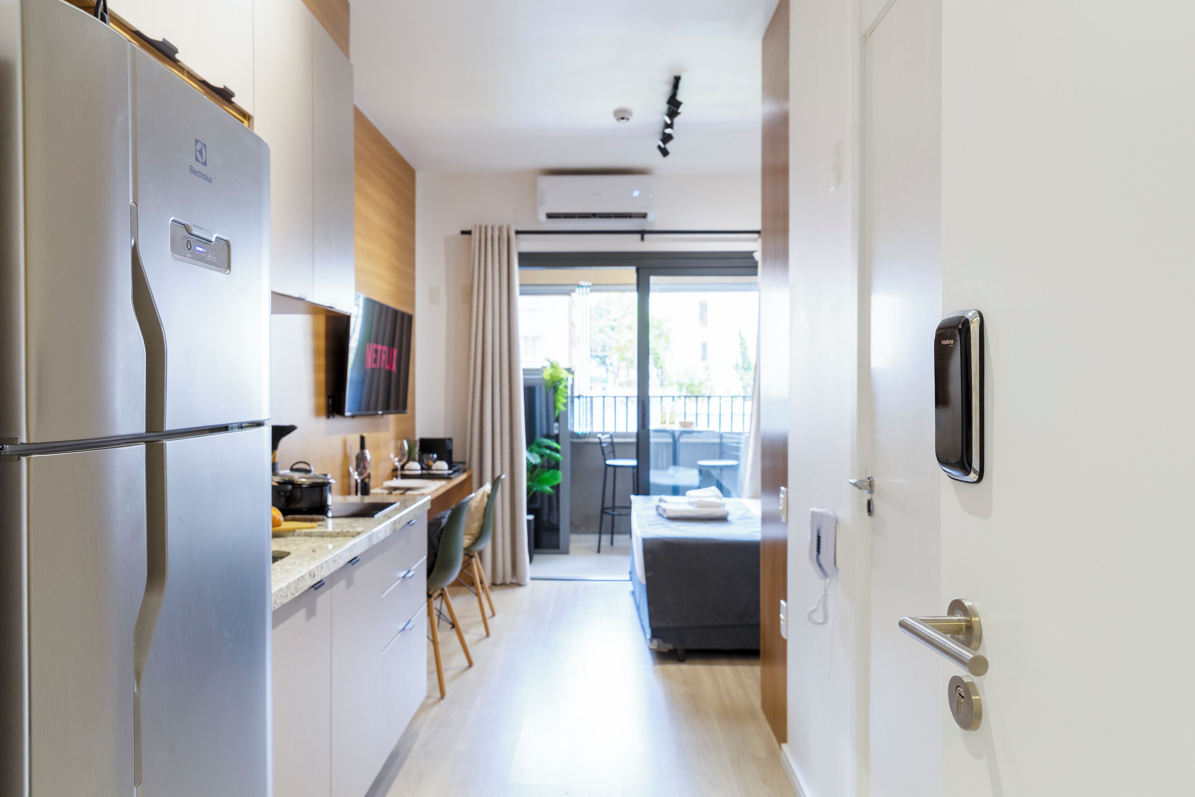 A modern kitchen with a refrigerator, a dining area with a table and chairs, and a view of the outside balcony.
