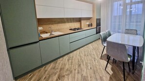 A modern kitchen with a wooden countertop, a sink, and a stove. There is a dining table with chairs and a window with curtains. - River View (Raionul Soroca)