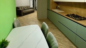 A modern kitchen with green cabinets, a white countertop, and a gas stove. There is a dining area with a white table and chairs. - River View (Raionul Soroca)
