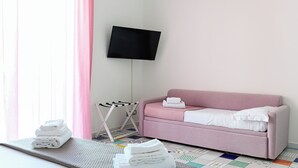 Una habitación con un sofá rosa, un televisor de pantalla plana montado en la pared, un tendedero y un suelo estampado.