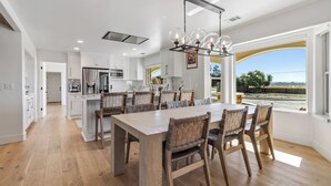 A modern kitchen with white cabinetry, a large island, and a dining area with a wooden table and chairs.