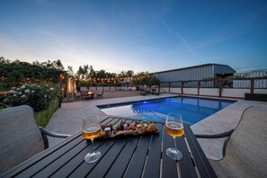 An outdoor pool area with a table set for drinks and snacks, surrounded by lounge chairs and a covered seating area.