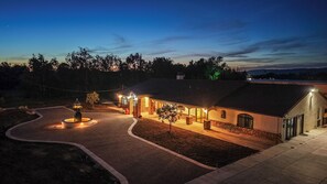 A house with a paved driveway, a fountain, and a well-lit exterior at dusk.