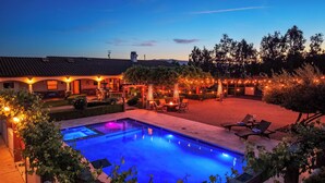 A swimming pool with a patio area, outdoor seating, and string lights.